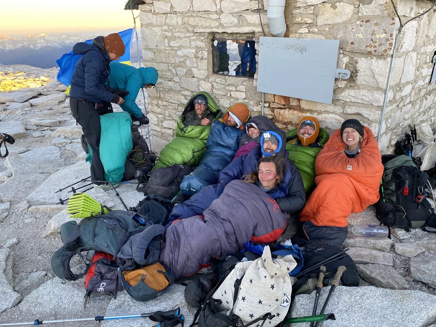 a group of hikers huddled together on top of a mountain their sleeping bags