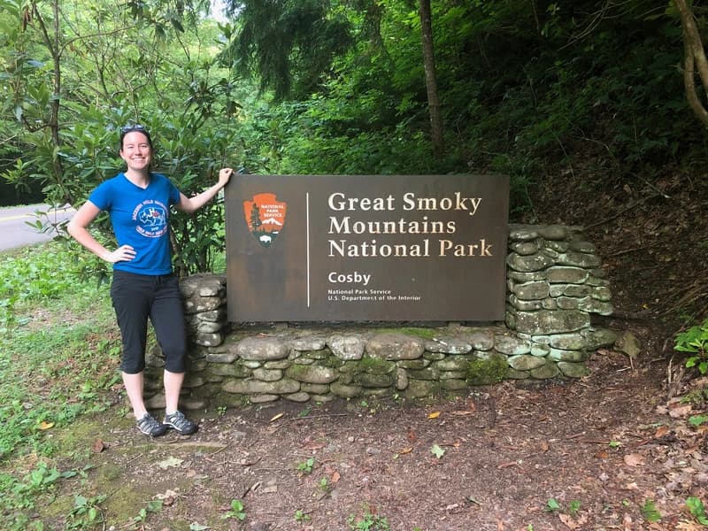 a woman in front of the great smoky mountains national park sign