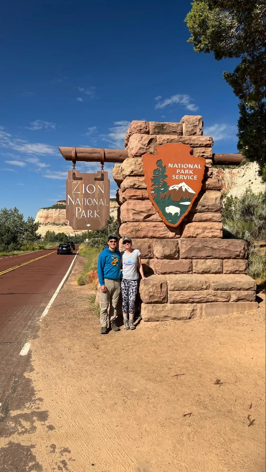 two people standing in front of the zion national park sign